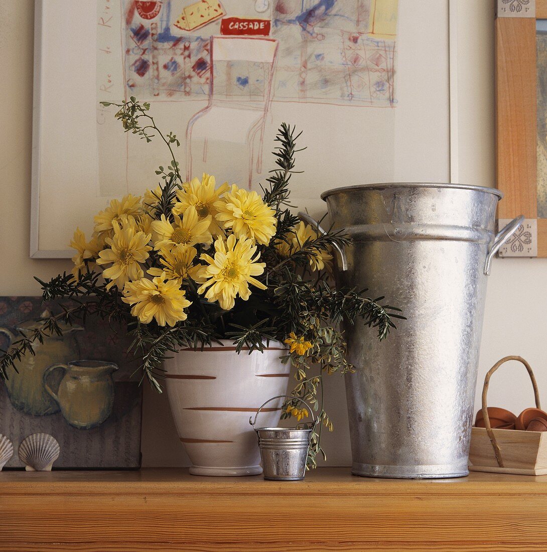 Eine Nahaufnahme von einem Blumentopf mit gelben Chrysanthemen, der neben einer Metall-Vase steht