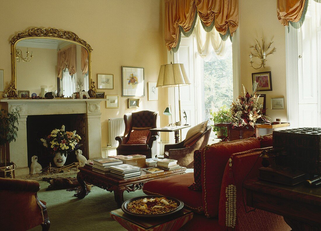 In einem Wohnzimmer mit getrimmten apricot Vorhängen hängt ein großer vergoldeter Spiegel über einen Marmorkamin