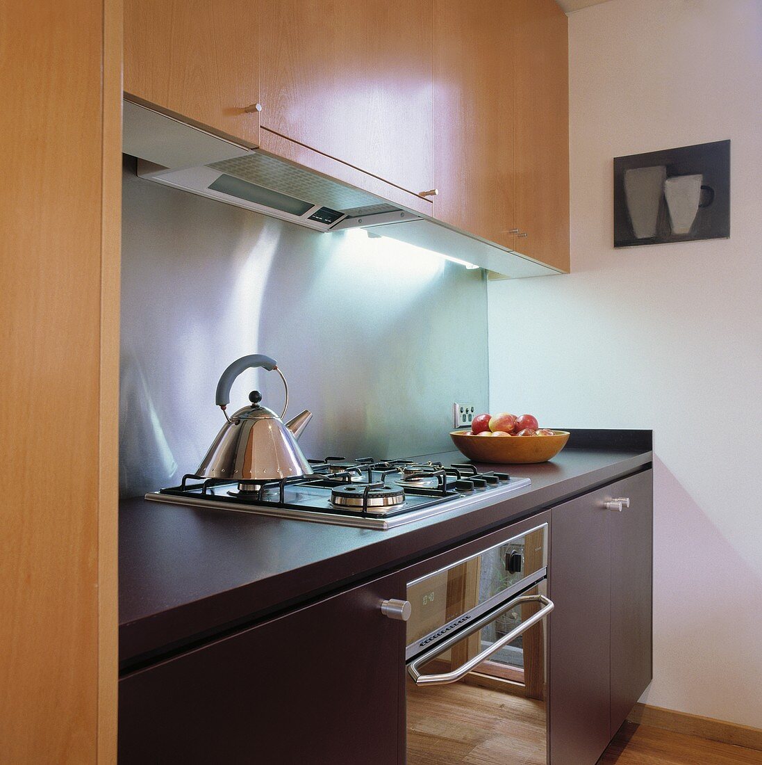 Eine kleine moderne Küche mit Holz-Einheiten und einer Edelstahl Rückwand