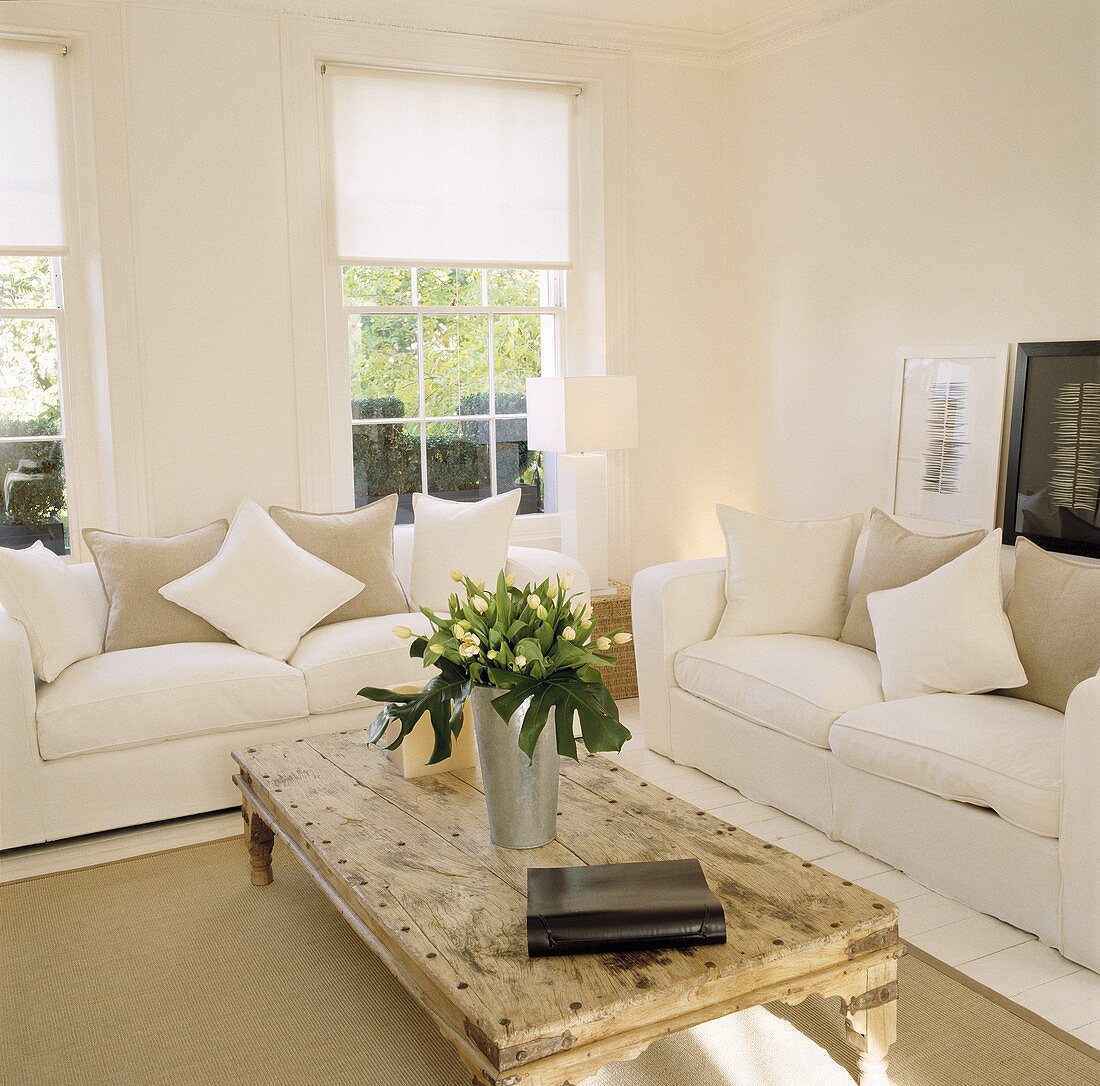 Weisses, modernes Wohnzimmer mit gemütlichen Sofas und rustikalem, altem Couchtisch