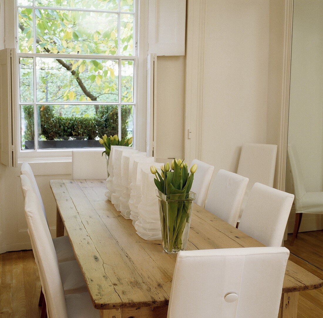 Weisses Landhaus-Esszimmer mit gepolsterten Stühlen um alten Holztisch und Blick in den Garten