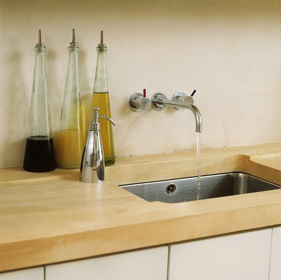 Küchenarbeitsfläche aus Holz mit eingefrästem Ablauf in Edelstahl-Unterbaubecken und moderner Wandarmatur neben Flaschen mit Essig und Öl