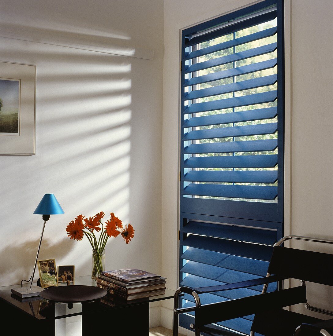 Sitzecke mit schwarzem Stahlrohrsessel aus der Bauhauszeit und halbgeschlossener blauer Jalousie vor bodentiefem Fenster