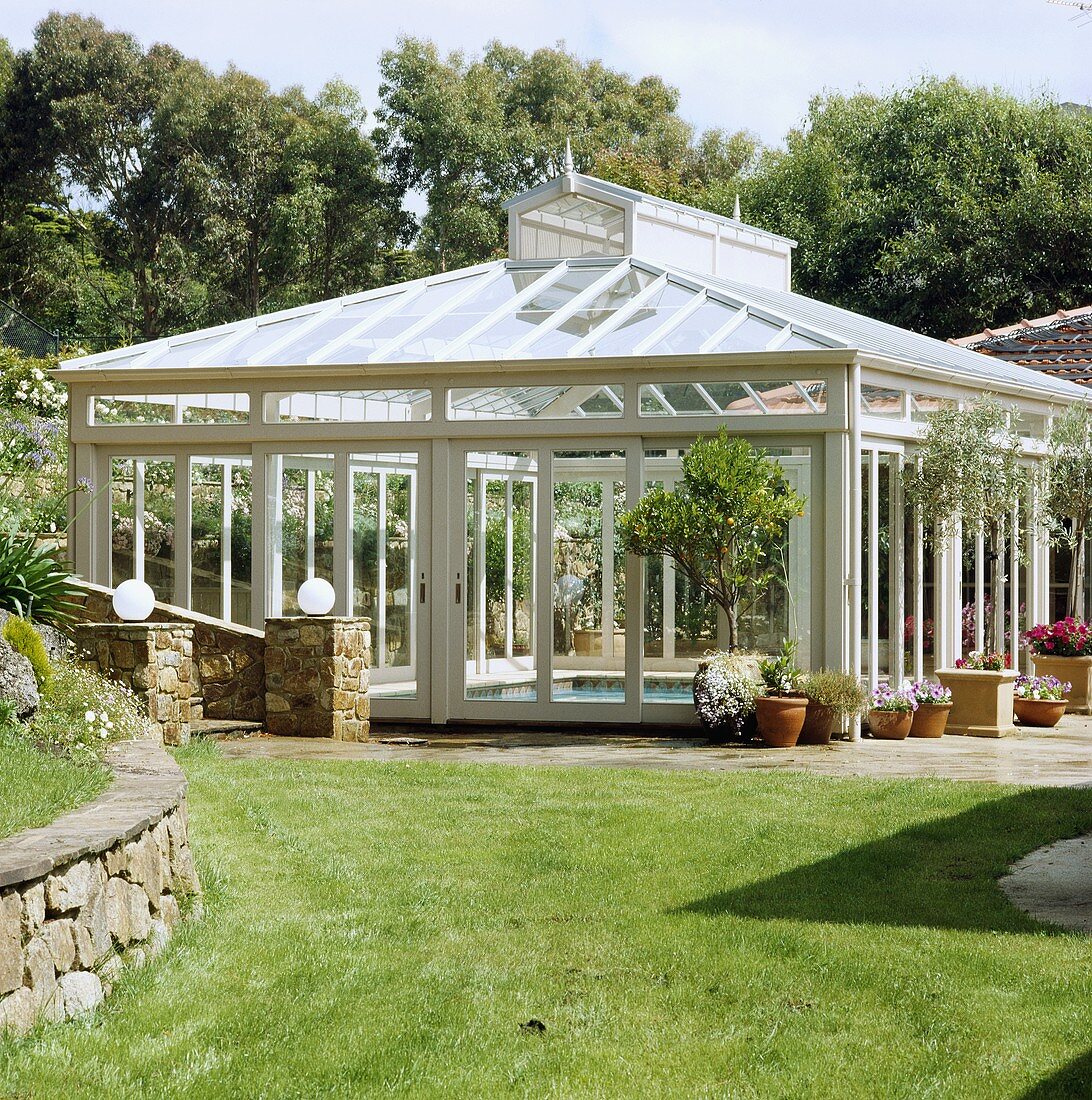Ein freistehender Glasbau, der das Schwimmbecken im Garten vor Witterung schützt