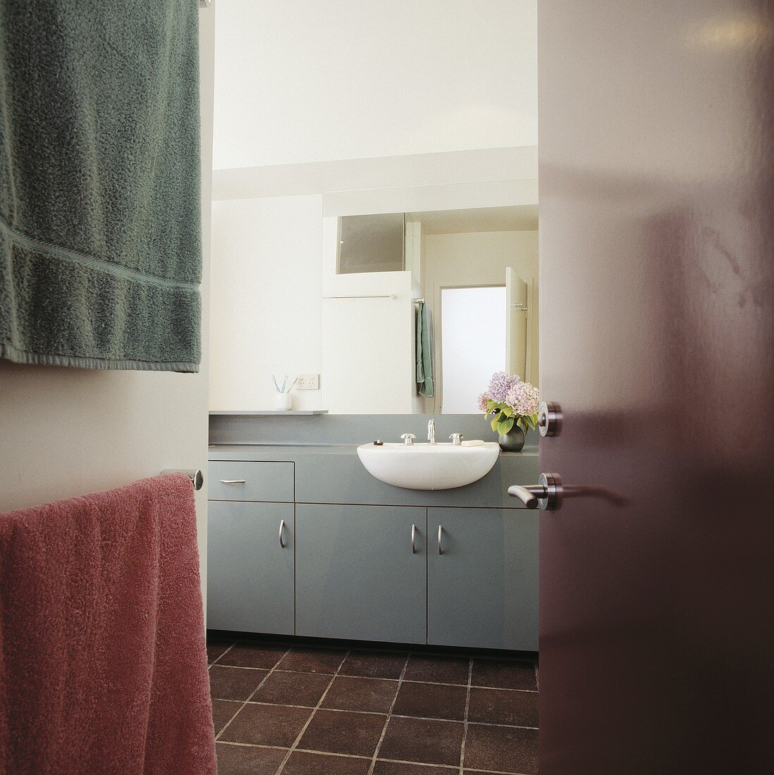 Blick durch bordeauxrote Tür auf bordeauxroten Fliesenboden in modernem Bad mit grauen Unterschränken