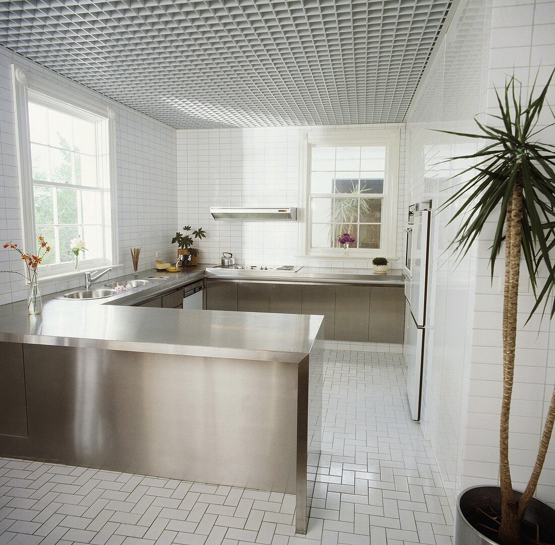 Edelstahl-Einbauschränke in steriler Küche mit weissen Fliesen an Wänden und Boden und weisser Rasterdecke