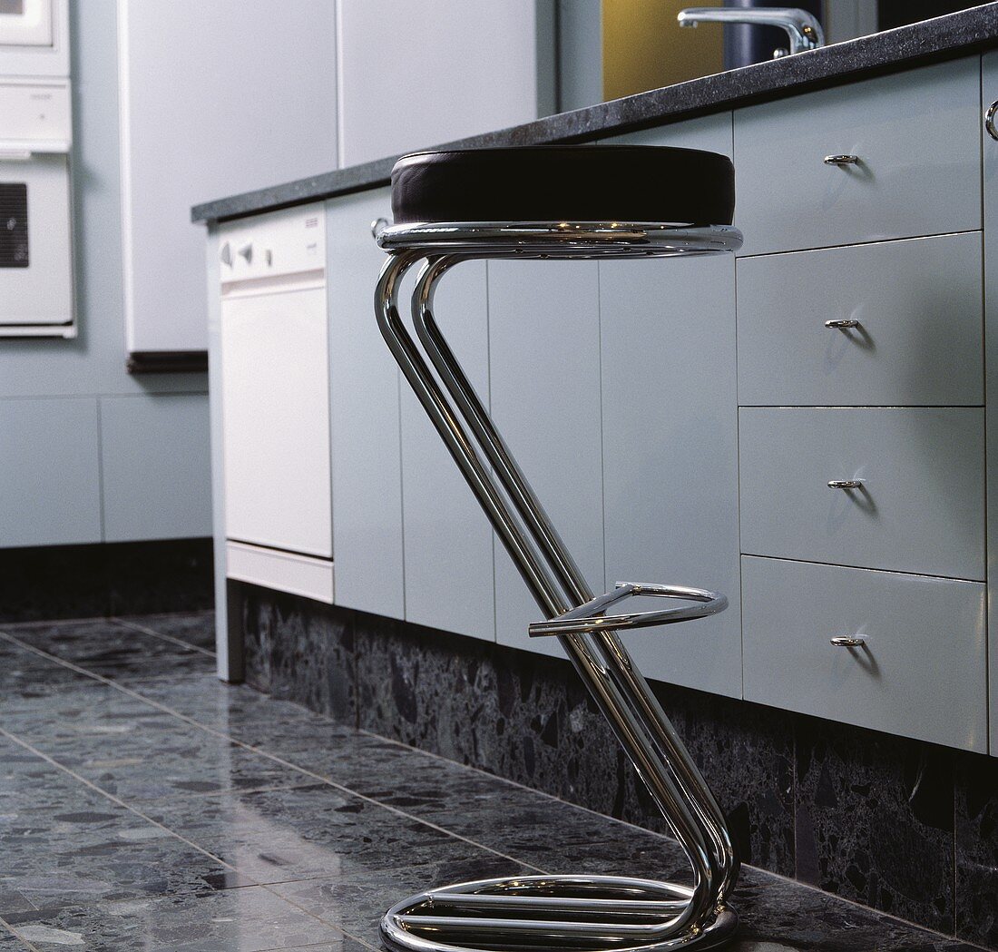 Nahaufnahme eines modernen Barhockers mit verchromtem Stahlgestell und Lederpolster in moderner Küche in Grauschattierungen