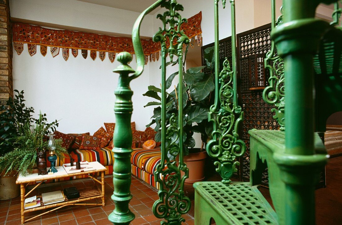 Grün lackierte, antike Metalltreppe in 60er-Jahre Wohnzimmer mit indischen Stoffen in Sofa-Ecke