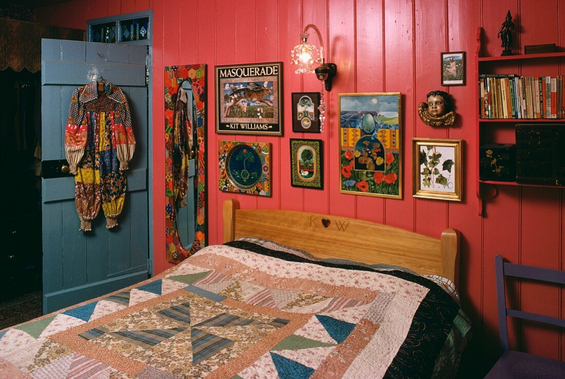 Schlafzimmer mit farbenfrohen Bildern auf rosa Wandtäfelung hinter Bett mit Patchwork-Decke in kleinem Hippie-Landhaus