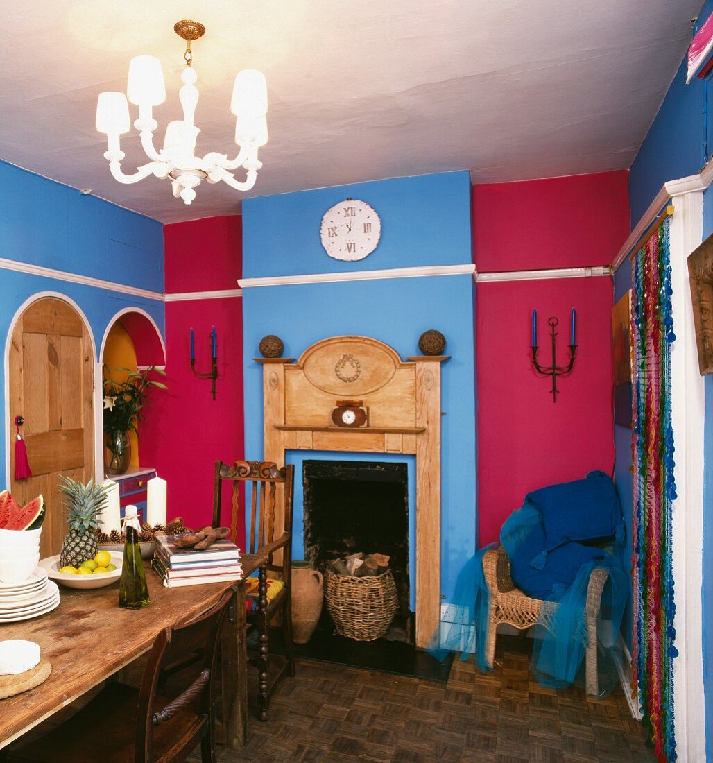 Stilmix in einem Esszimmer mit kräftigen Wandfarben in blau und rot und portikusartiger Holzumrahmung des Kamins