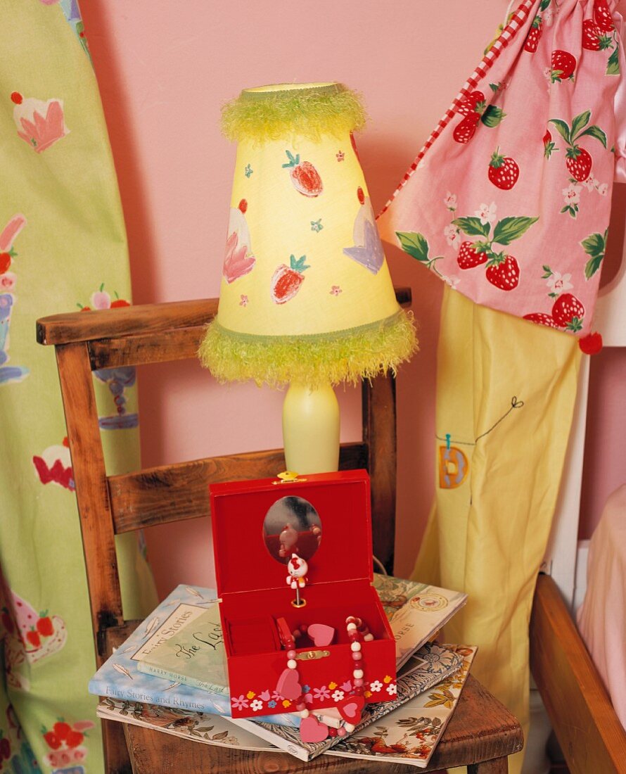 Stoffbeutel und Tischlampe mit gemalten Fruchtmotiven hinter rotem Schmuckkästchen auf hölzernem Kinderstuhl