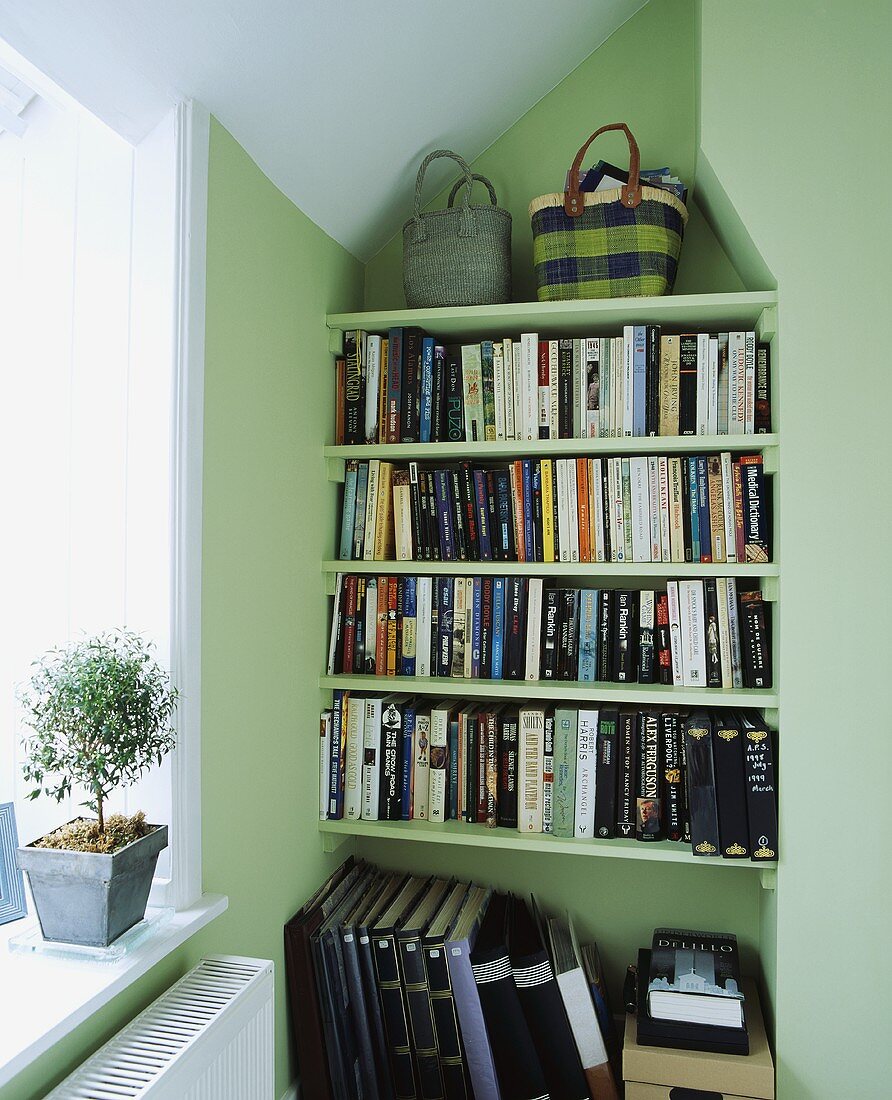 Strohtaschen in Blautönen vor lindgrüner Wand auf Bücherregal in Wandnische mit Licht von der Seite
