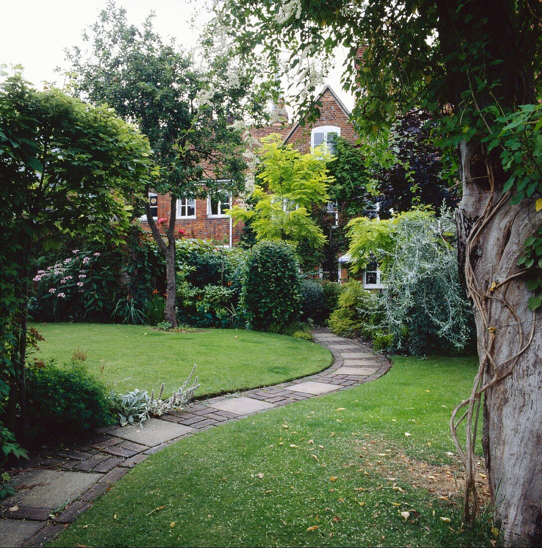 Schmaler, gepflasterter Weg in der Rasenfläche eines parkartigen, englischen Gartens