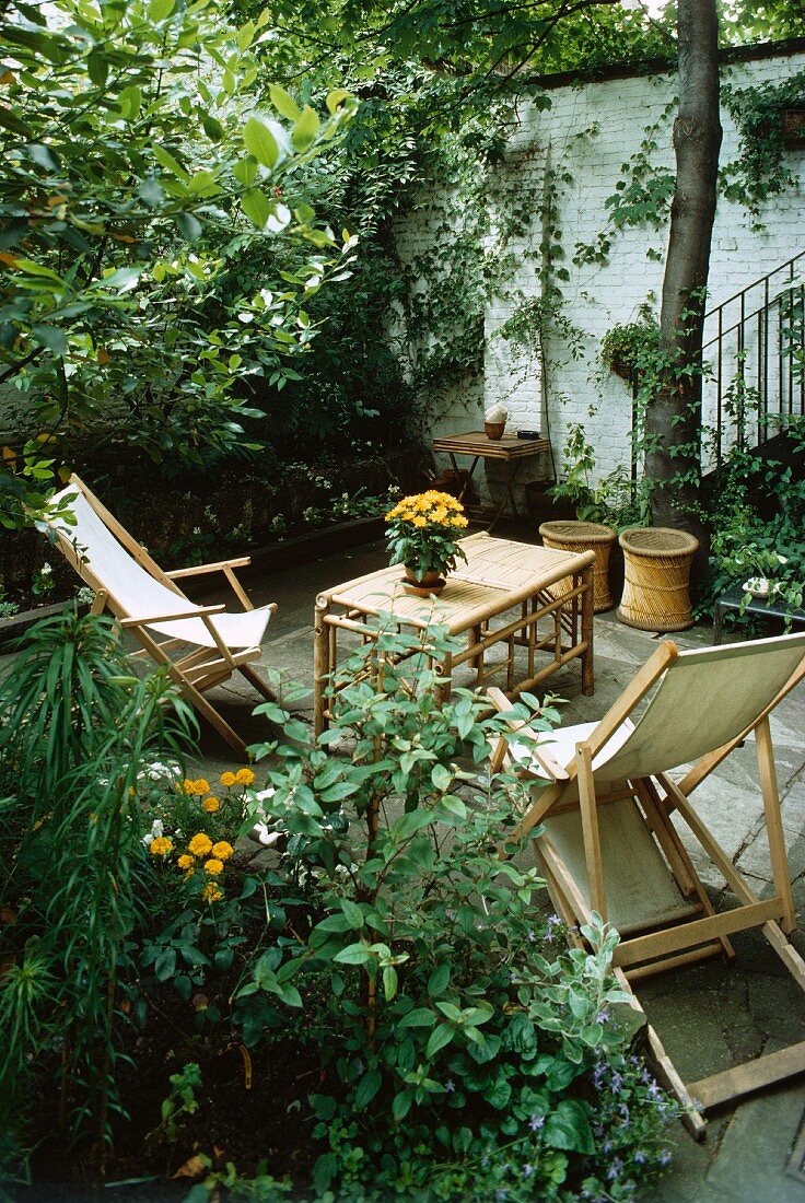 Holzliegestühle mit Tisch auf geschützter Terrasse in Sommergarten