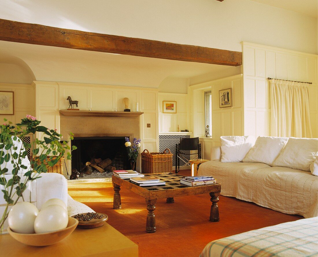 Breite, helle Sofas und rustikaler Couchtisch aus Holz in grosszügigem Wohnzimmer mit cremefarbener Holzvertäfelung