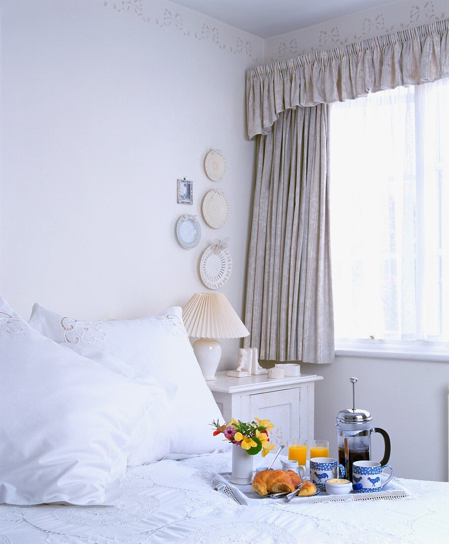 Frühstückstablett mit Kaffeebereiter auf Bett in weißem Schlafzimmer mit zarter Schablonenbordüre