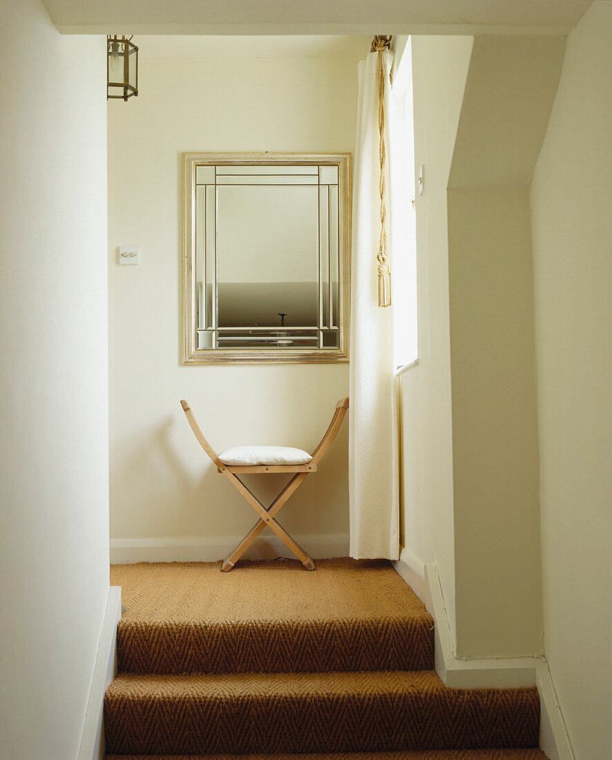 Treppenabsatz mit Sisalteppich und hölzernem Scherenstuhl unter Spiegel mit geometrischer Verzierung