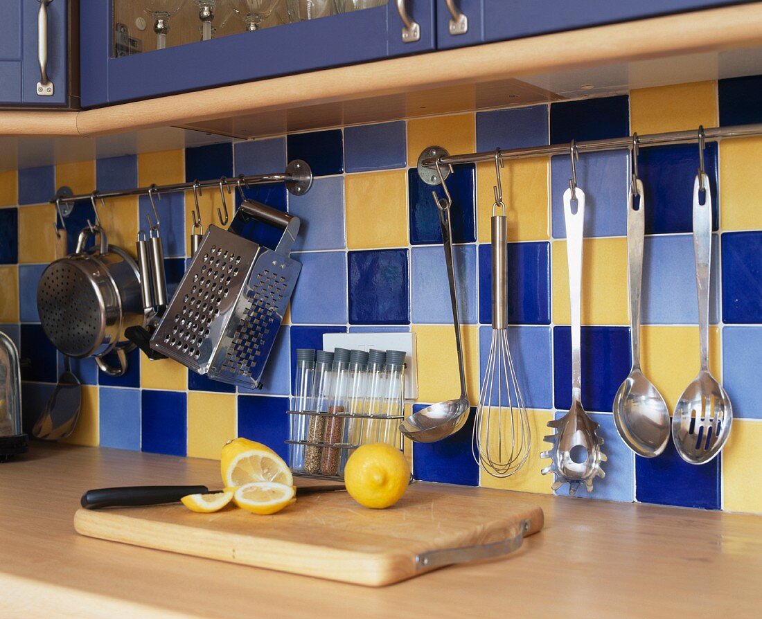 Küchenutensilien an einer Stange mit Fleischerhaken aufgehängt vor gelb und blau gefliester Rückwand