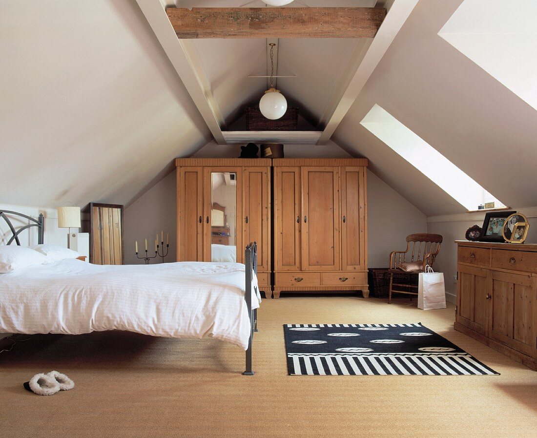 Schlafzimmer unterm Dach mit grossen Fenstern in der Dachschräge, rustikalen Möbeln aus Kiefernholz und Metallbett