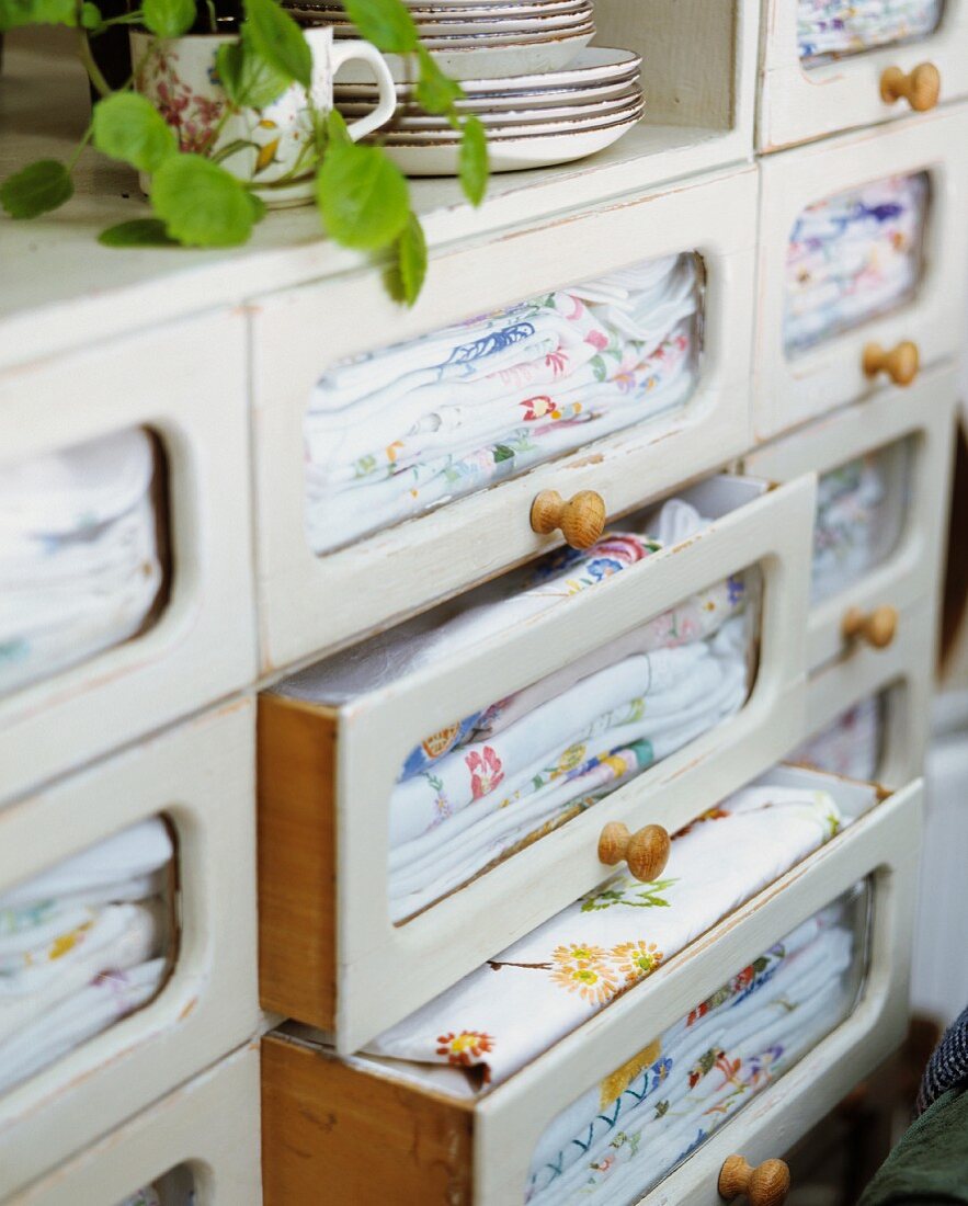 Bestickte Stoffe in Schubladen mit Glasfronten in weißem, altem Küchenschrank