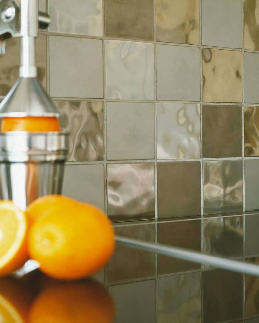 Nahaufnahme von Metallic-Fliesen hinter Küchentheke mit Ständerpresse für Orangen