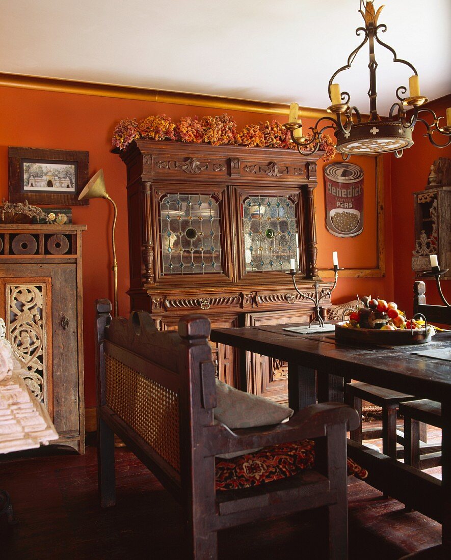 Antike, dunkle Holzmöbel in Esszimmer mit terracottafarbenen Wänden und vielen Sammlerstücken