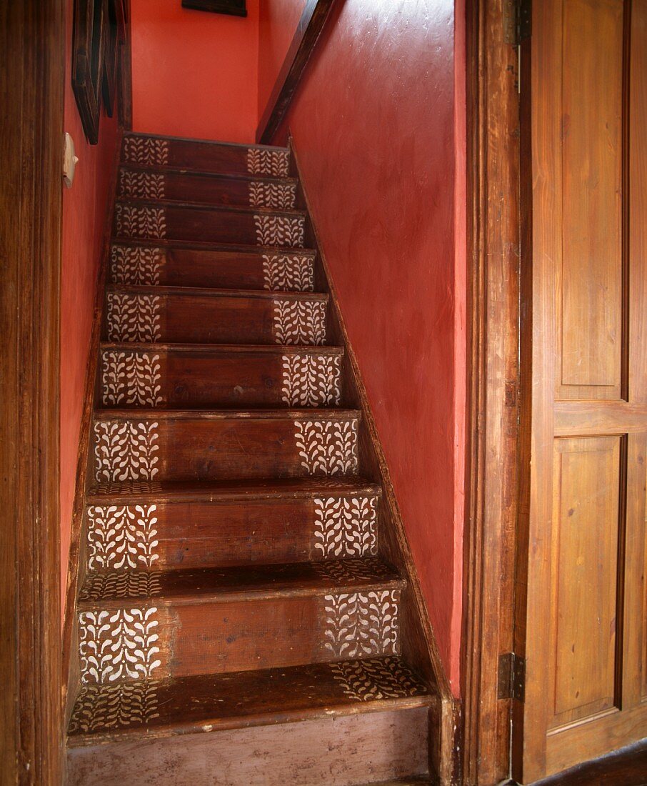 Weisses, kleines Muster in Schablonentechnik auf den Stufen einer Holztreppe zwischen Wänden in kräftigem Rosa