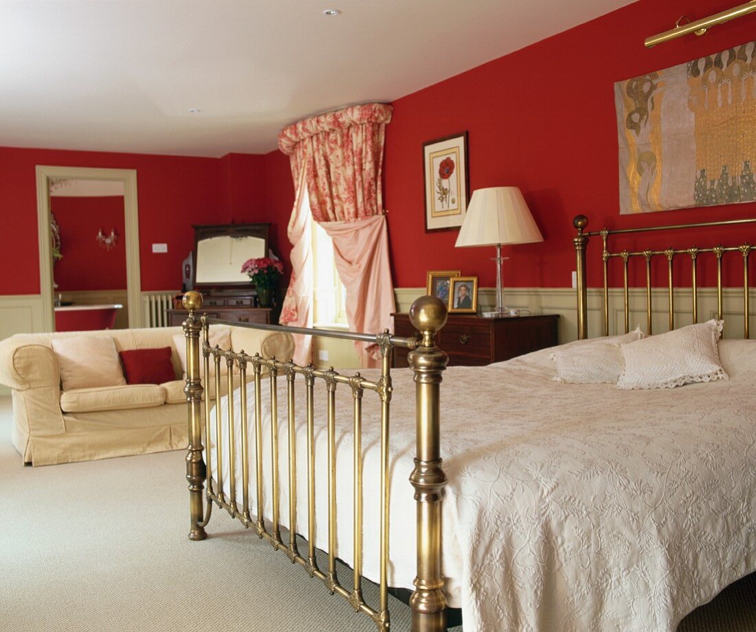 weiße Tagesdecke auf antikem Messingbett in elegantem Schlafzimmer mit roter Wand und heller Holzvertäfelung