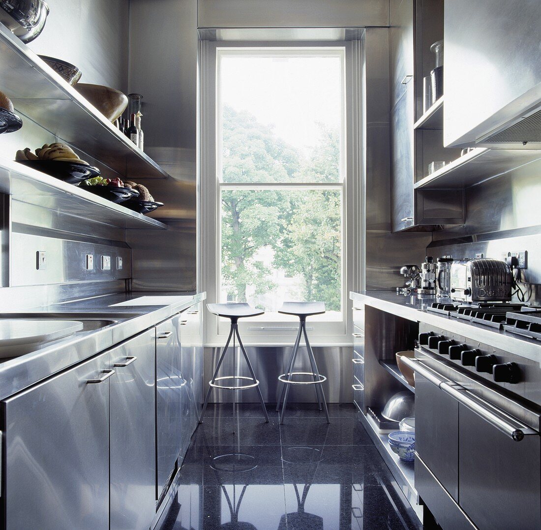 Metallhocker vor einem hohen Fenster in der modernen Küche mit Edelstahl-Einbauschränken