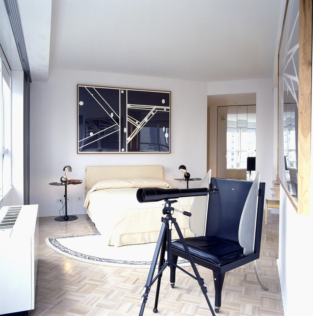 Weiß gestrichenes Schlafzimmer mit Bett mit cremefarbener Bettwäsche und darüberhängendem abstrakten schwarz-weiss Bild, dazu ein Teleskop und ein schwarzer Ledersessel