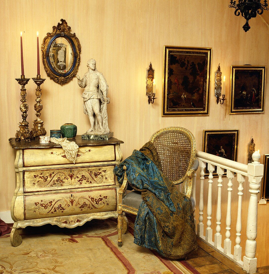 Galerie mit vergoldeter antiken Kommode, darauf hohe Kerzenhalter und eine Statue, daneben ein vergoldeter antiker Stuhl
