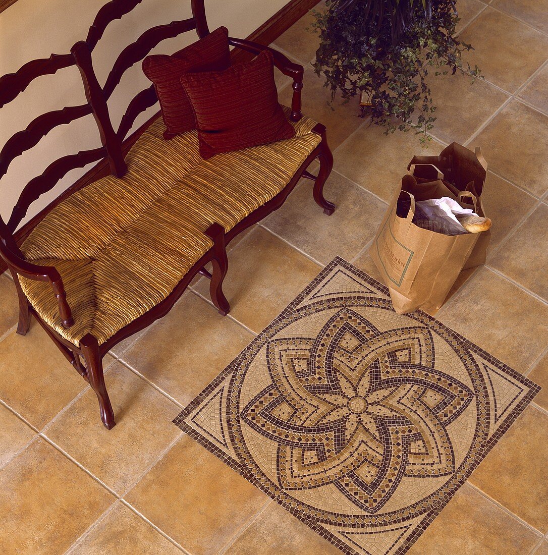 Holzbank mit Strohsitz auf einem Fliesenboden mit kunstvollen Mosaik-Mustern