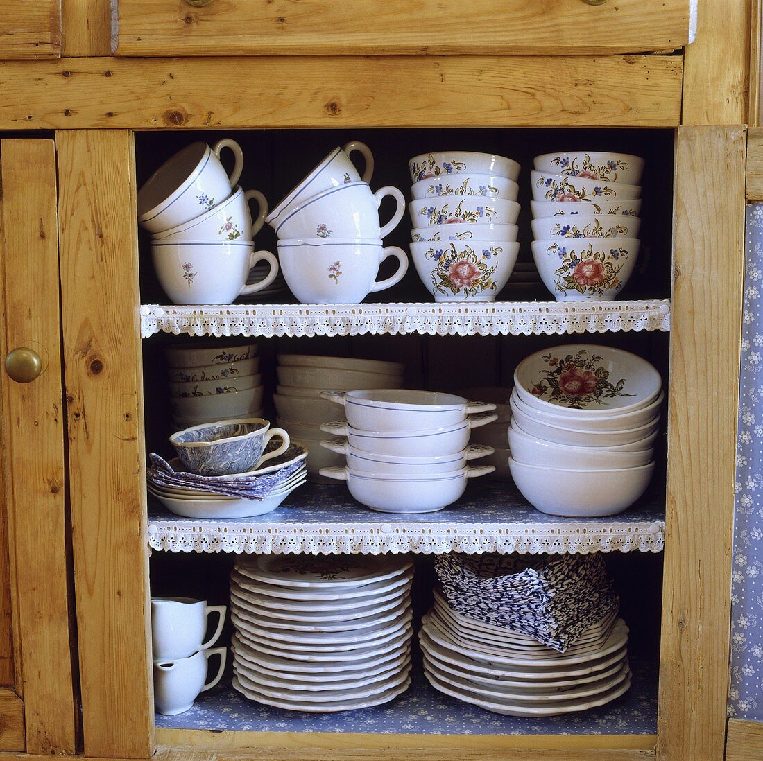 Porzellantassen und Teller auf Regalen in einem Holzschrank