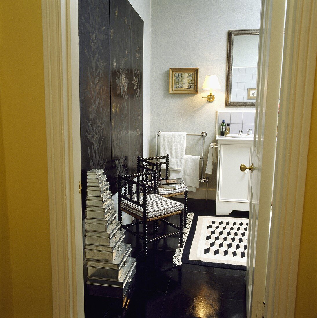Blick in ein schwarz-weisses Badezimmer mit gestapelten Aluminiumdosen neben einem antiken Stuhl