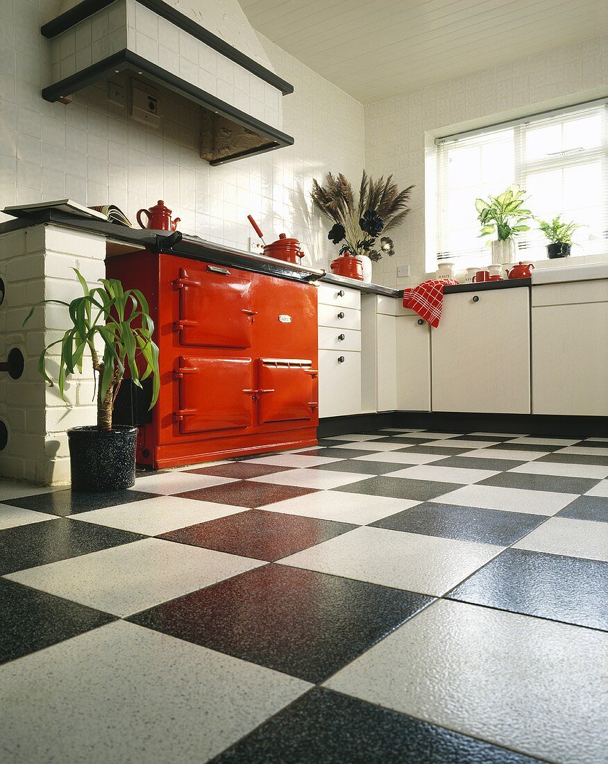 Schwarz-weiße Keramikfliesen, weiße Schränke und roter Ofen in einer Küche