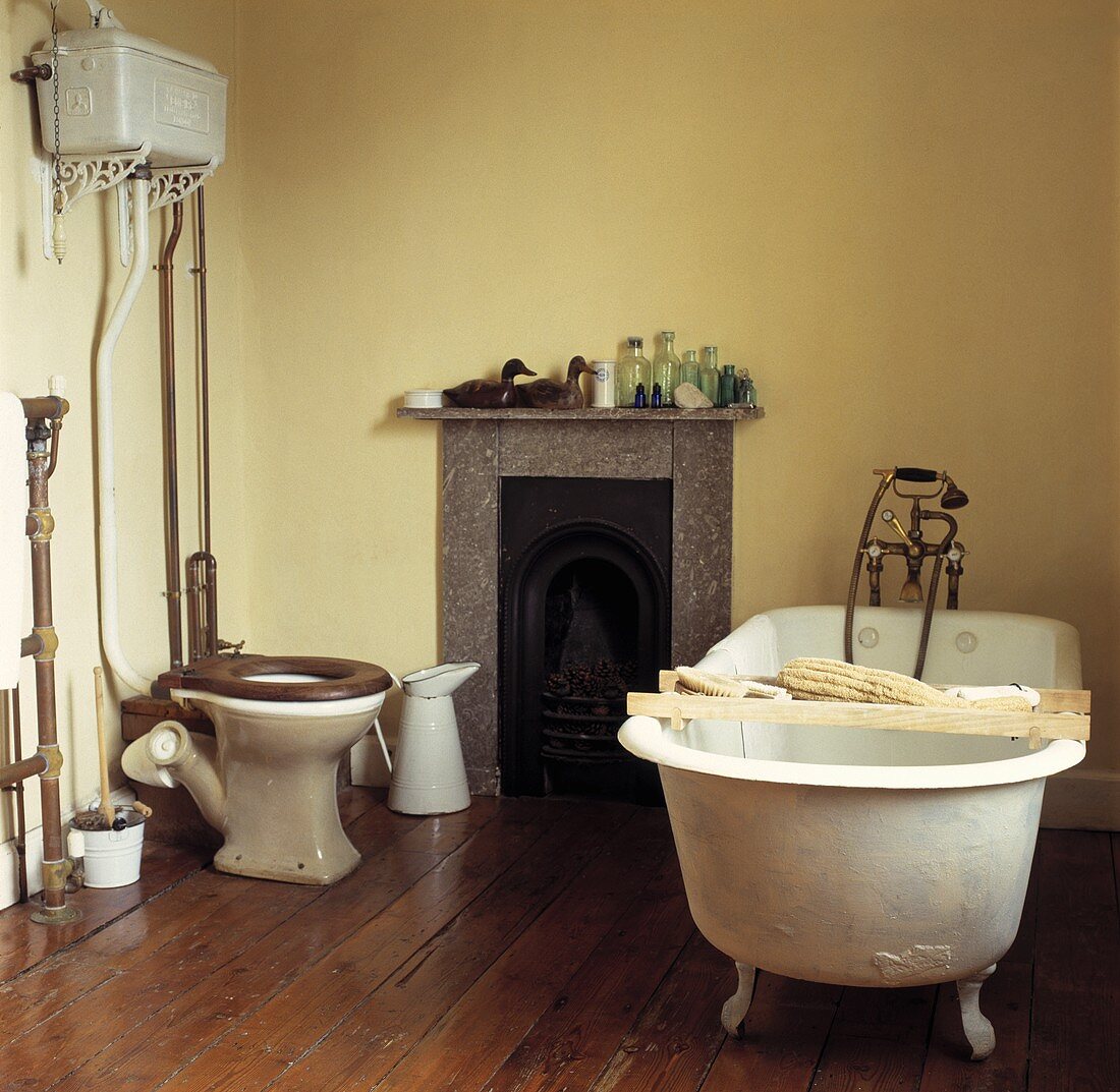 Frei stehende Badewanne mit Holzablage und Toilette in einem Badezimmer mit Holzboden und kleinem Kamin
