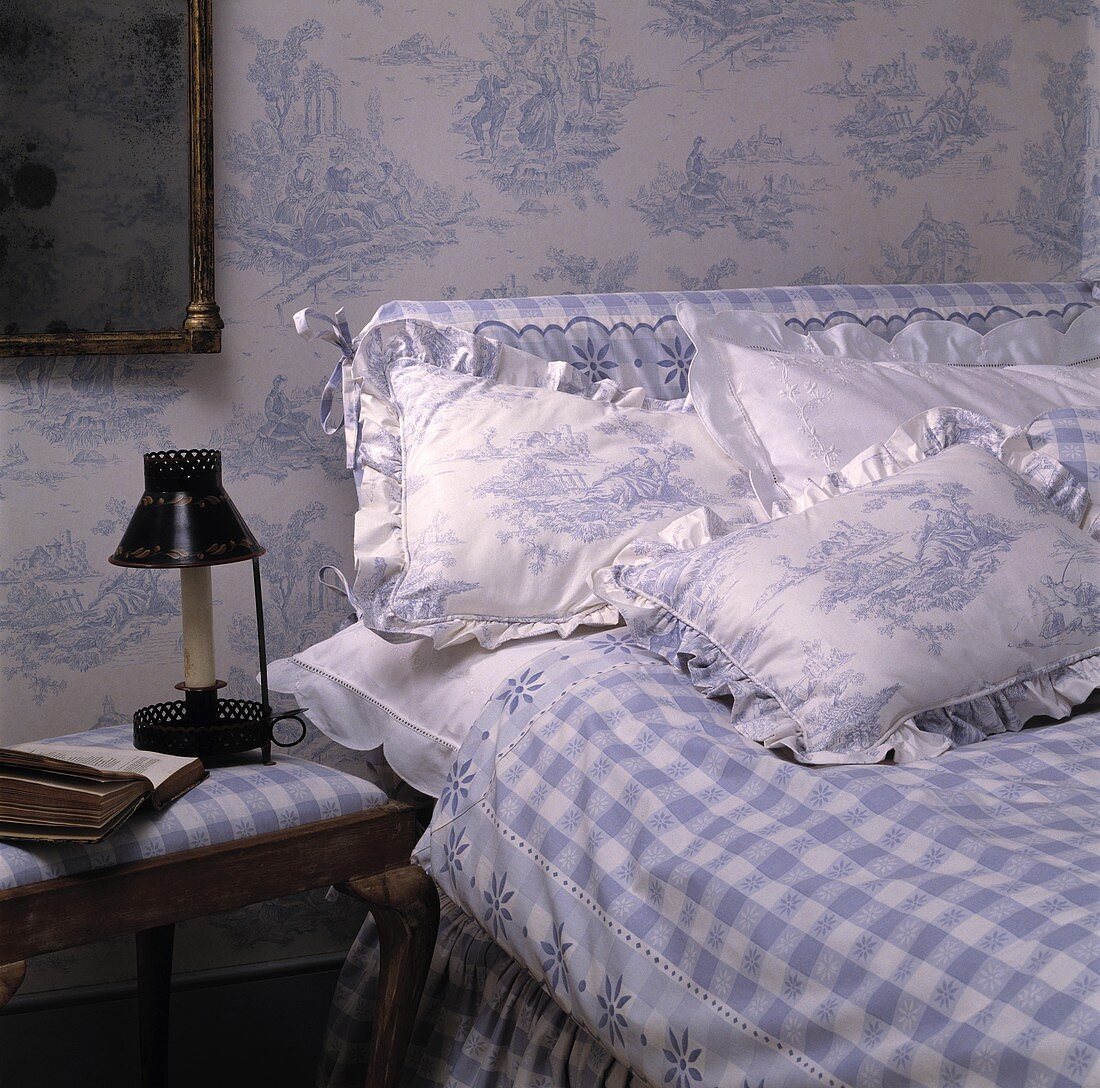 Tapete und Kissen mit dem gleichen Toile-de-Jouy-Muster und blau-weiss karierte Bettdecke in einem Schlafzimmer