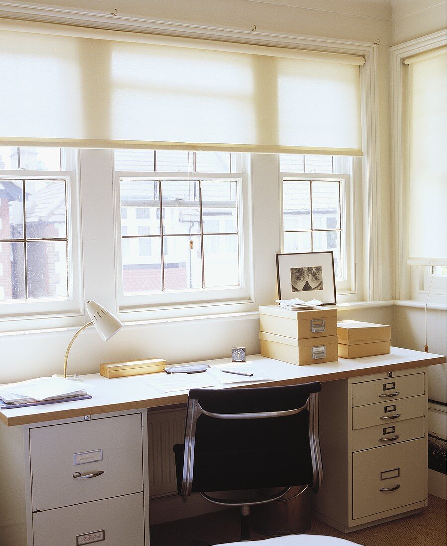 Home office mit Tischplatte aus Holz über Container und Schreibtischstuhl aus schwarzem Leder und Chrom vor Fensterfront
