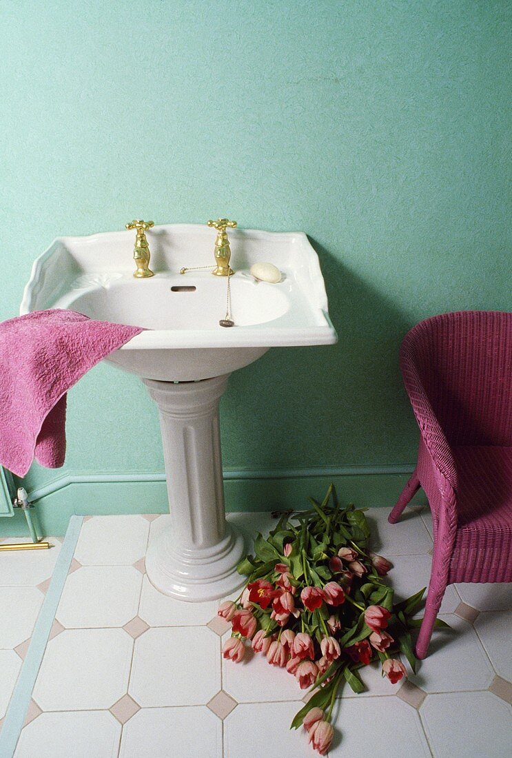 Vintage Standwaschbecken mit rosa Handtuch vor türkiser Wand und rosa Korbsessel neben Tulpen auf Boden
