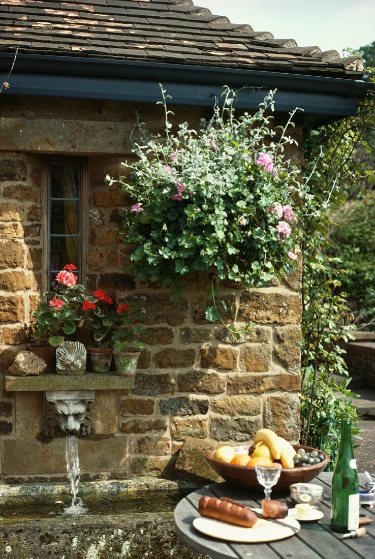 Frühstücken im Freien vor sonnenbeschienenem Steinhäuschen mit Blumentöpfen am Fenster und Wasserspeier unter Fensterbank