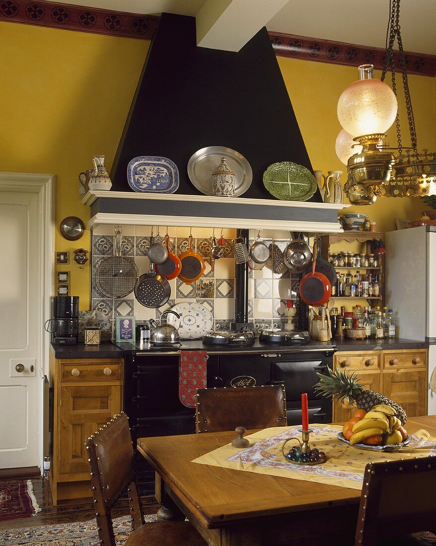 Wohnküche mit viktorianischer Glaslampe über dem Esstisch aus Kiefer, die Stühle mit Lederbezug
