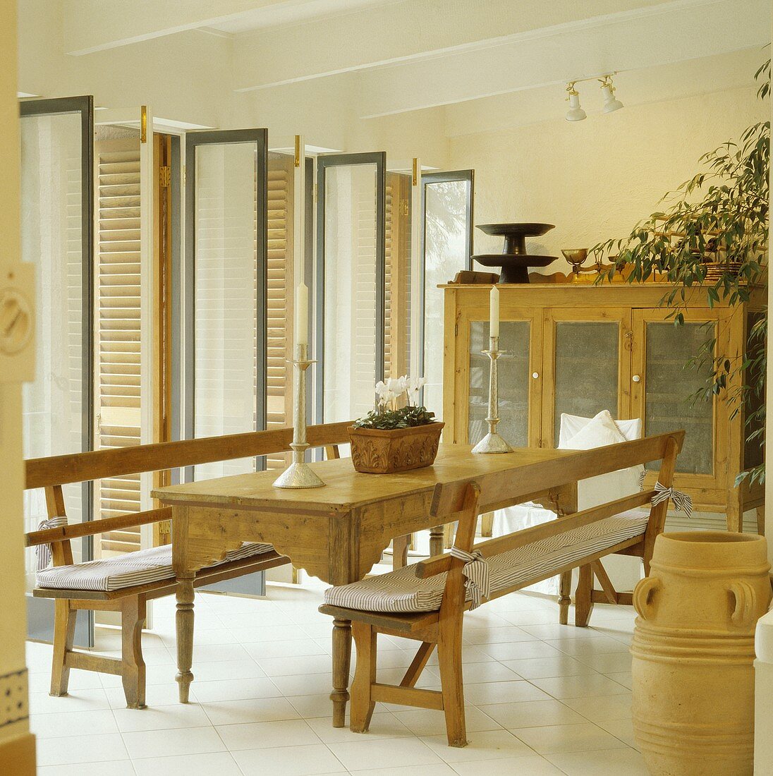 Rechteckiger Tisch und Bänke aus Kiefernholz in einem modernen weissen Esszimmer mit offenen Glastüren und Fensterläden
