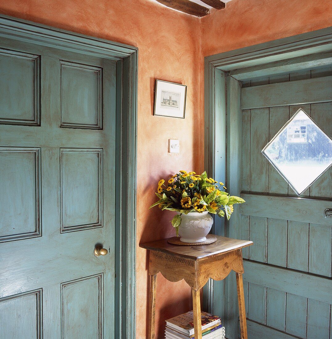 Ecke im Vorraum mit blaugrauen Türen und orangeroter Wand mit Blumenvase auf rustikalem Blumenständer