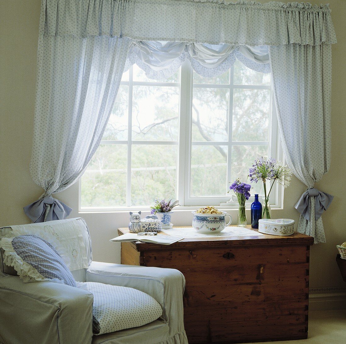 Weisser Sessel und eine Truhe neben dem Fenster mit Voile-Vorhängen