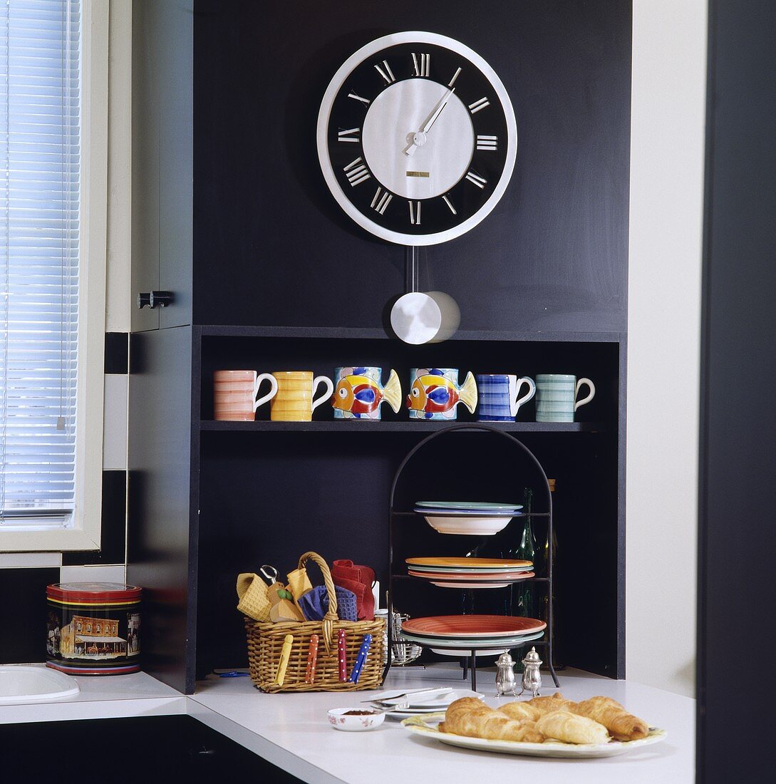 Wanduhr an schwarzem Küchenschrank über einem Regal mit bunten Keramiktassen
