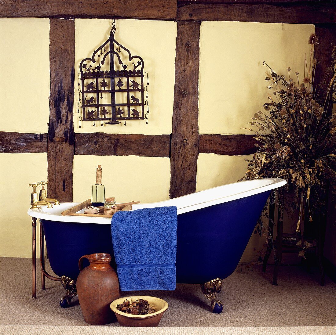 Freistehende Vintage Badewanne mit dunkelblauer Aussenwand und goldenen Füssen vor Fachwerkwand