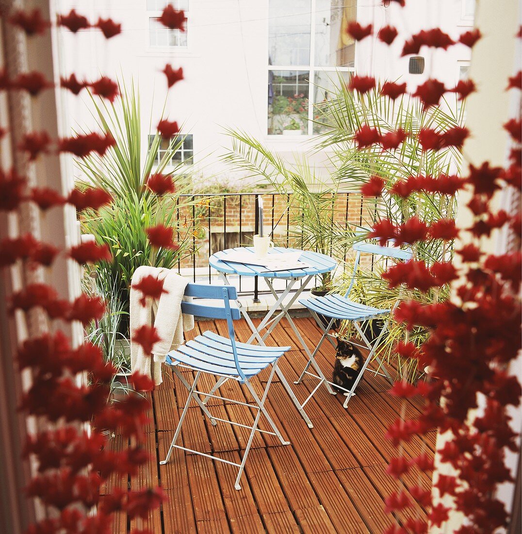 Blick durch Glastür auf Balkon mit blauen Gartenstühlen auf Holzterrasse