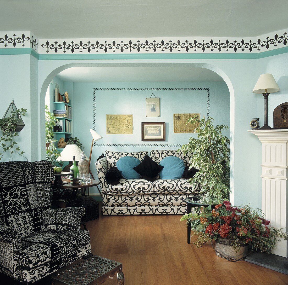 Mediterraner Wohnraum mit türkis getönten Wänden und schwarzweissem Ohrensessel vor offenem Durchgang mit Blick auf Sofa