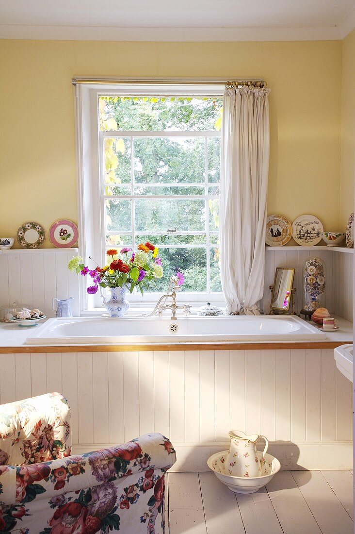 Traditionelles gelb getöntes Badezimmer mit weiß lackierter Holzverkleidung an Badewanne