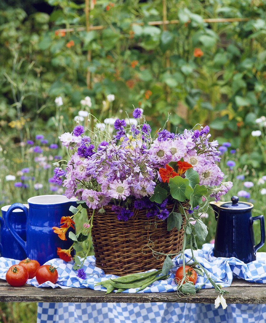 Wiesenblumen im Korb neben blauen Kannen auf dem Tisch